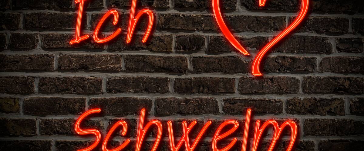 A neon sign spelling "Ich Schweim" on a brick wall.