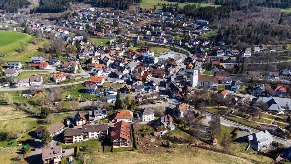 A densely populated village with a prominent church, surrounded by green fields and residential buildings.