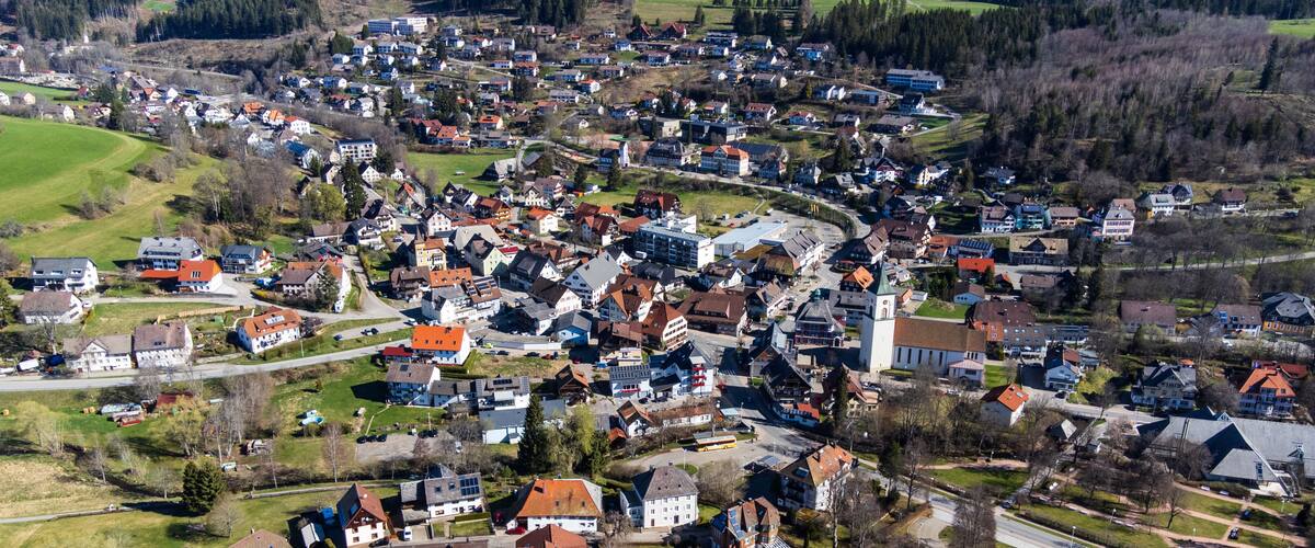 A densely populated village with a prominent church, surrounded by green fields and residential buildings.