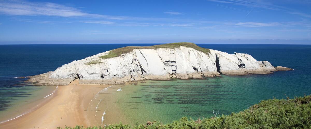 A coastal landscape with a sandy beach, white cliffs, and clear blue waters.