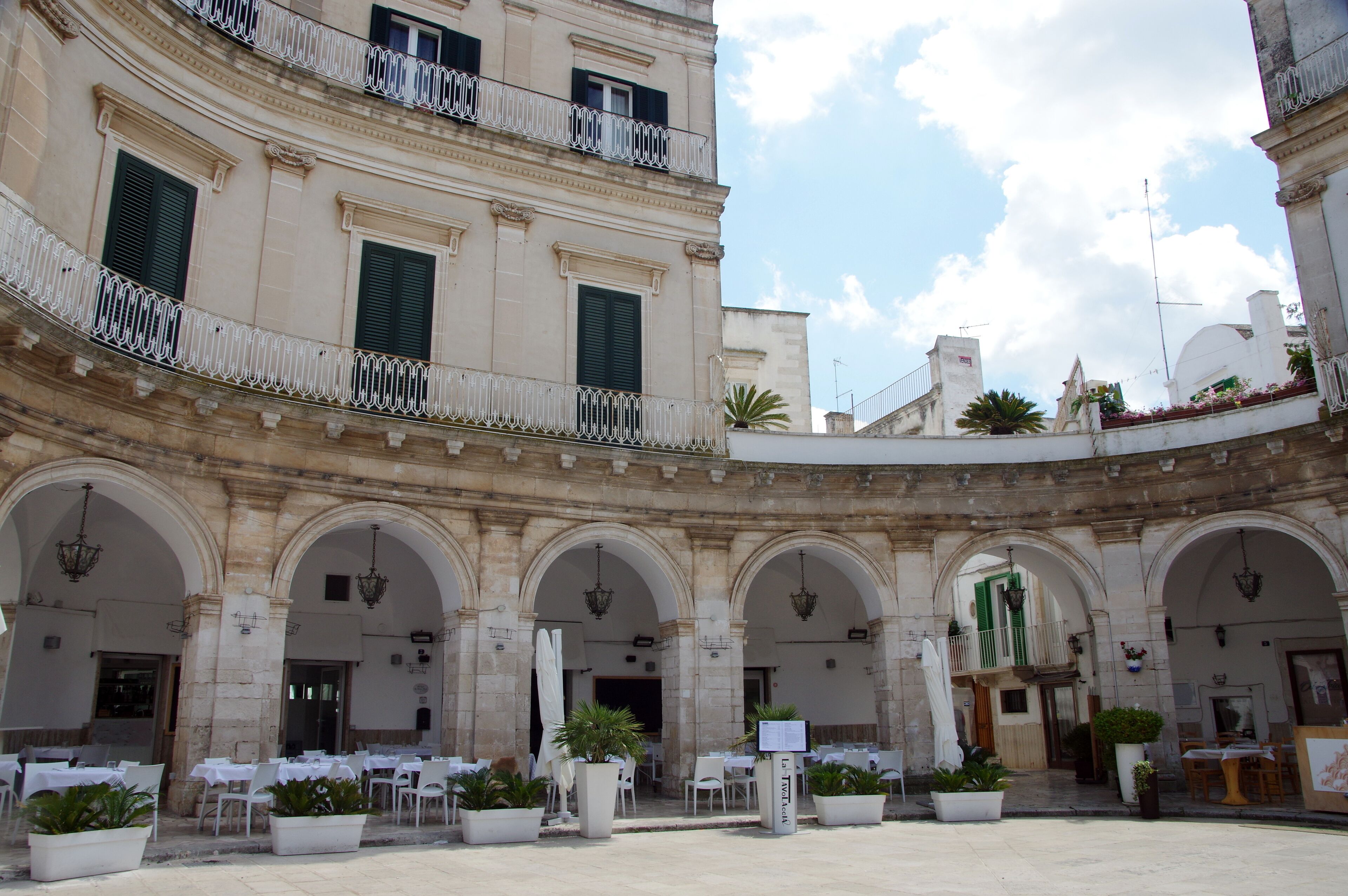 A historic courtyard with arches, outdoor seating, and potted plants.