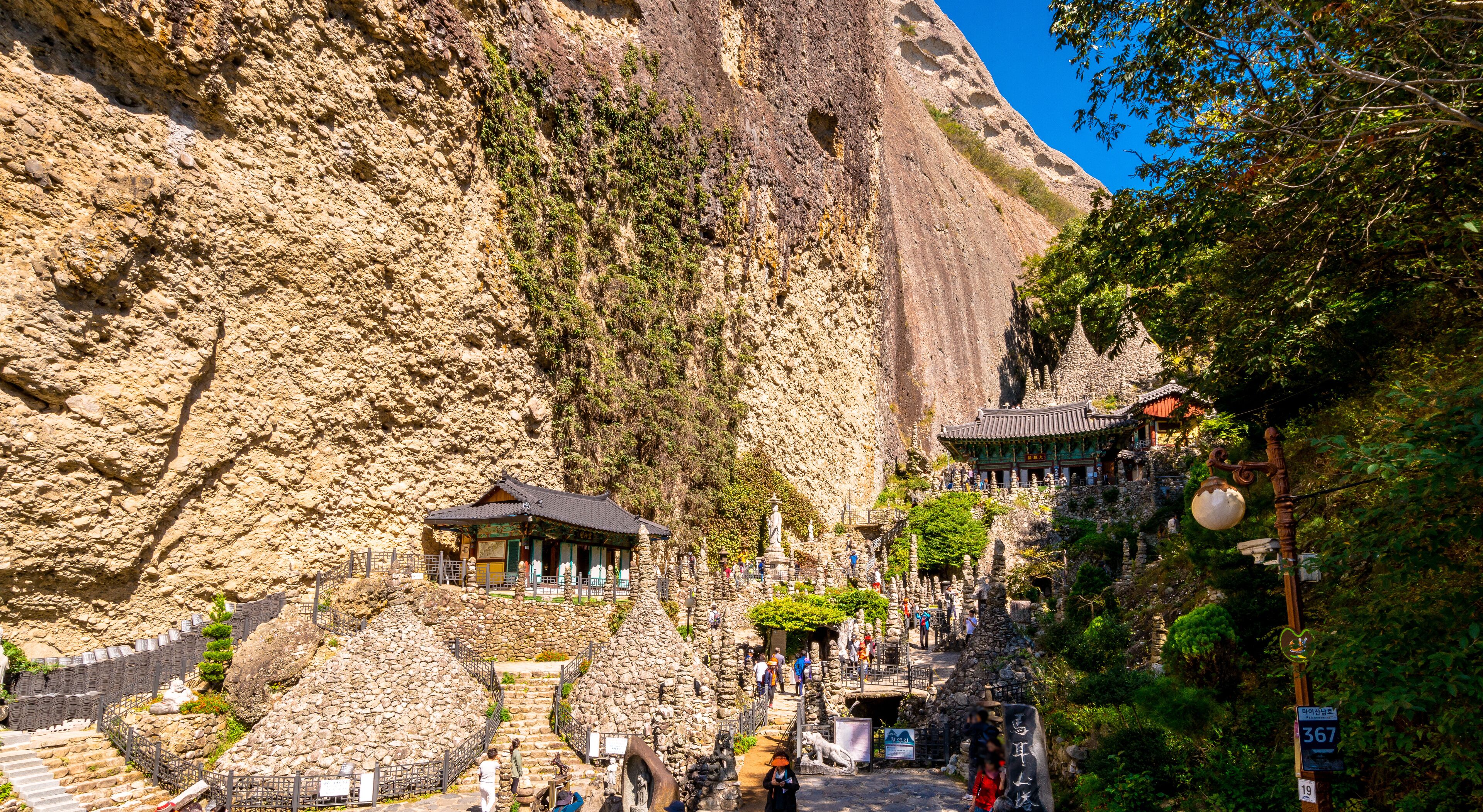 A traditional temple nestled in a rocky mountain landscape with a steep cliff and a stone staircase leading up to it.