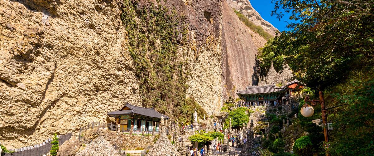 A traditional temple nestled in a rocky mountain landscape with a steep cliff and a stone staircase leading up to it.