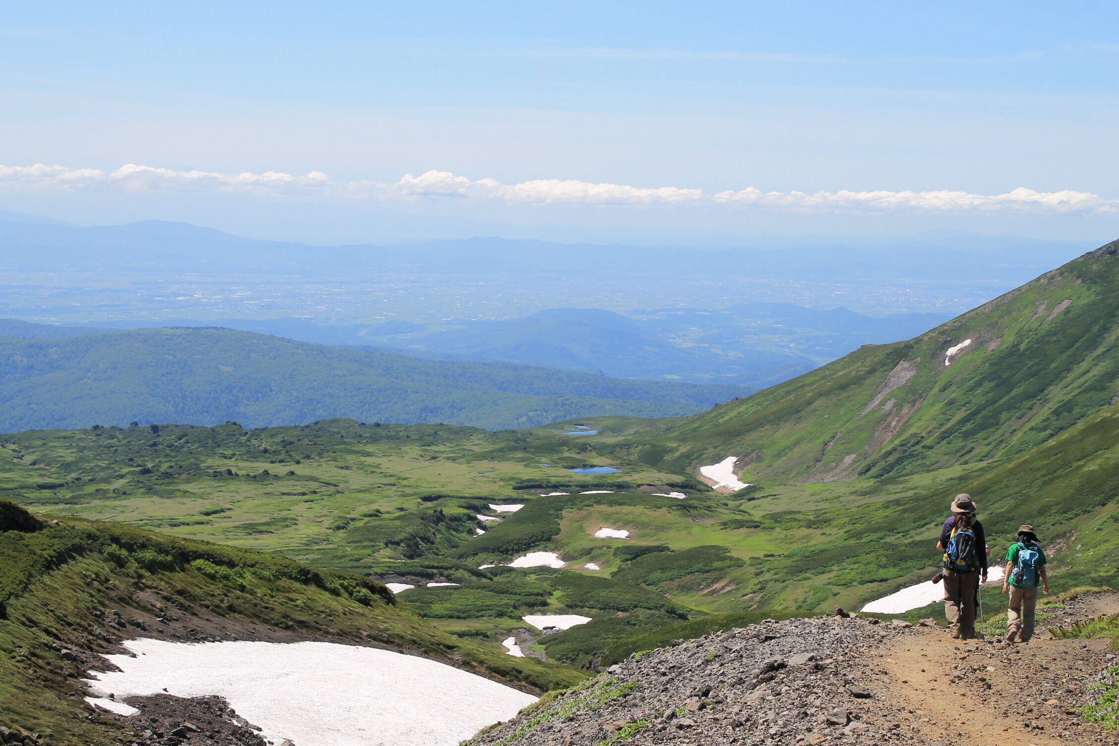 A mountainous landscape with hikers, green valleys, and a distant lake.