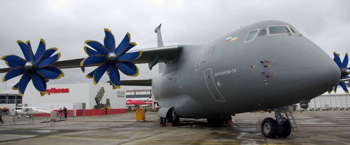 A large military transport aircraft with blue and yellow propellers on the wings, parked on a tarmac.