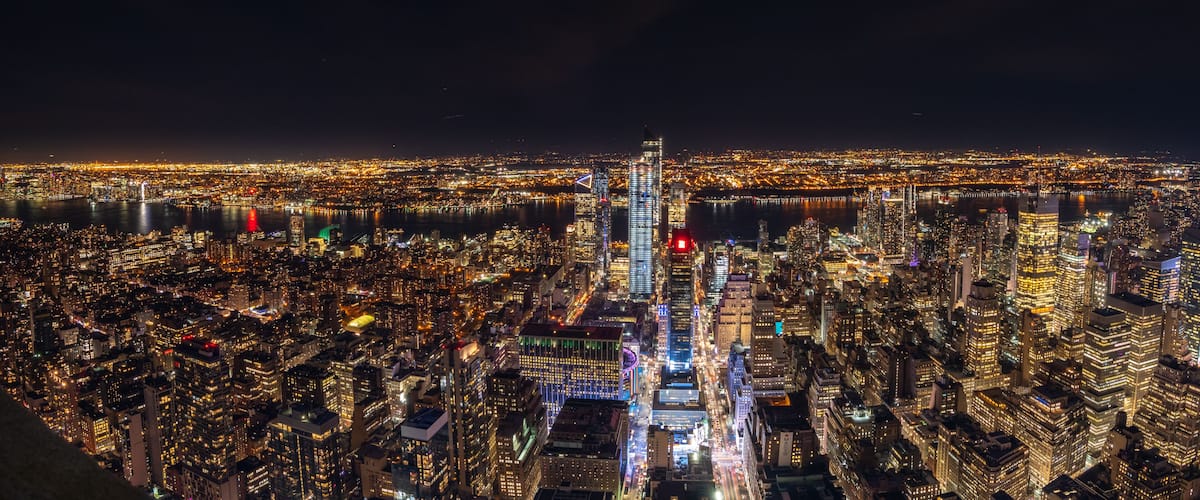 A nighttime cityscape with a prominent skyscraper, dense urban buildings, and a river.