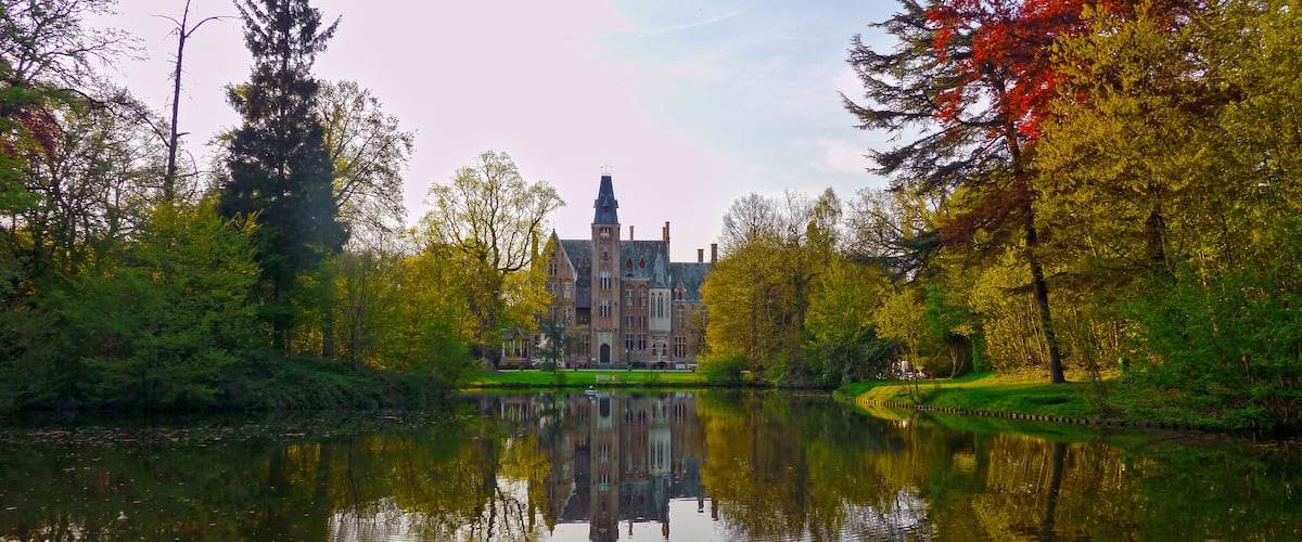 A historic building reflected in a calm lake, surrounded by autumn-colored trees.