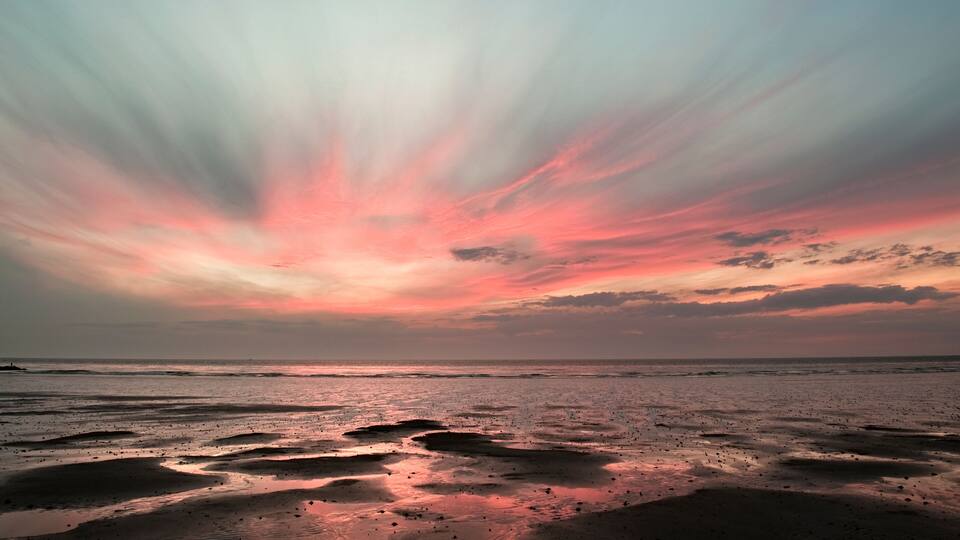A beach with wet sand and a sunset sky.