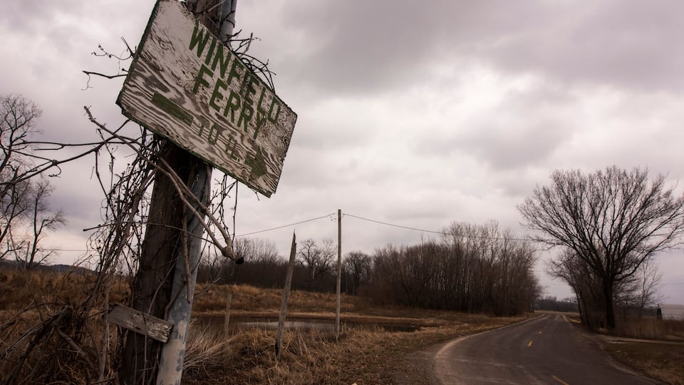 A rural road with a damaged signpost and leafless trees.