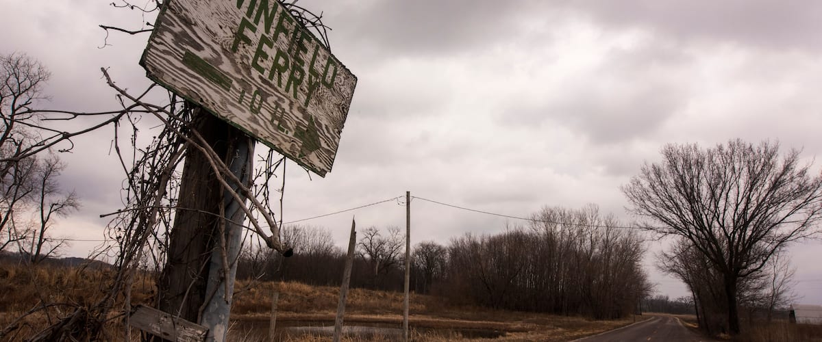 A rural road with a damaged signpost and leafless trees.