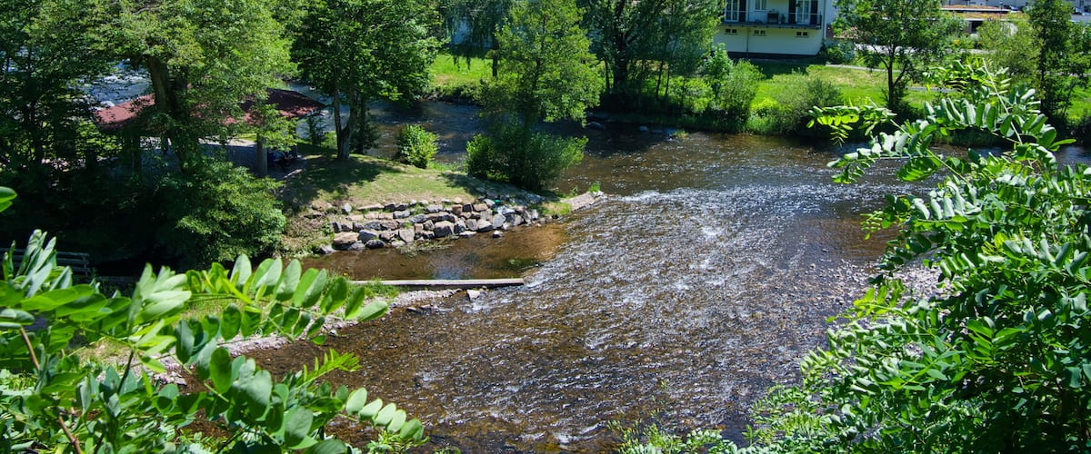 A river flowing through a valley with lush greenery and traditional buildings in the background.
