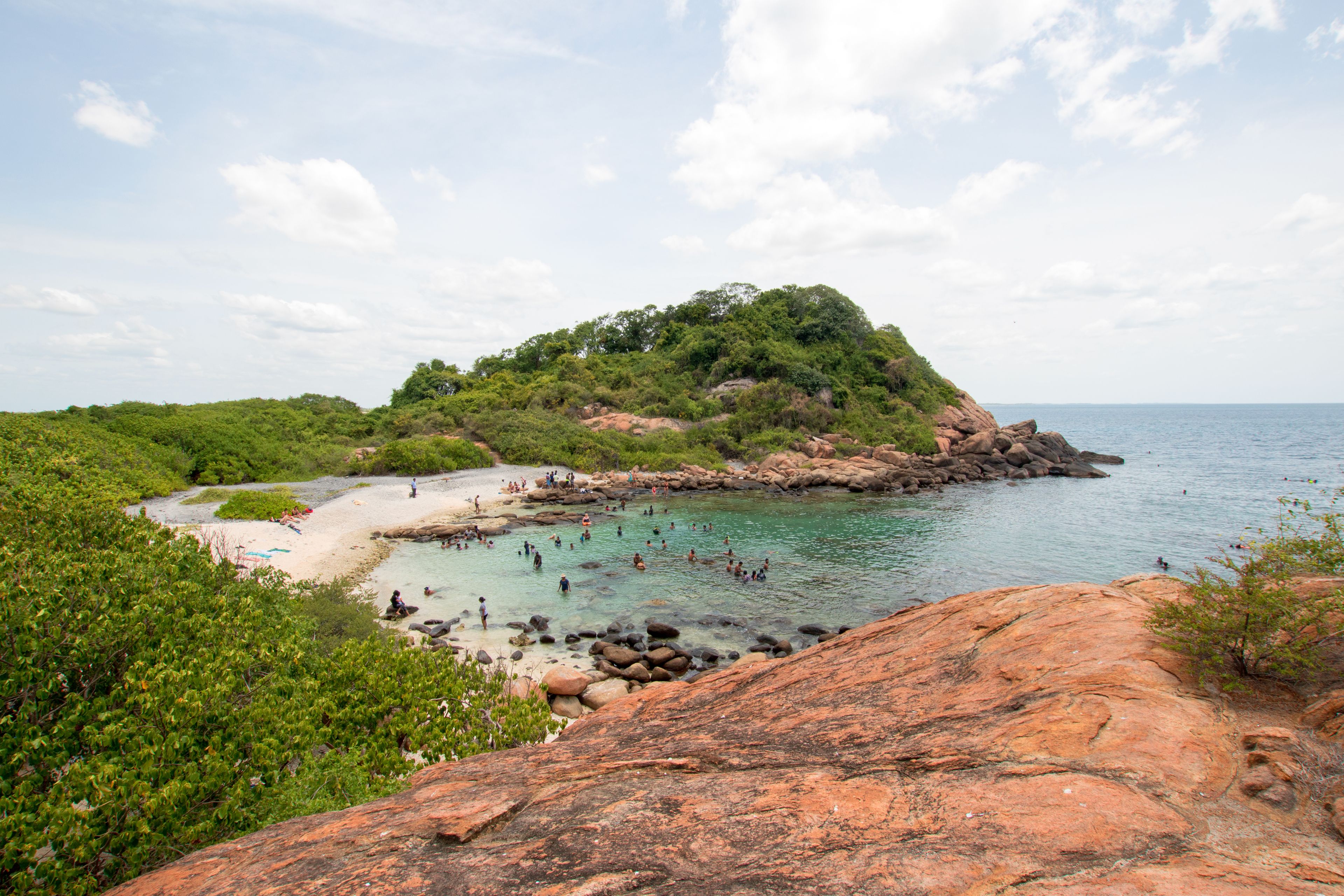 A coastal landscape with a rocky outcrop, clear turquoise water, and lush greenery.