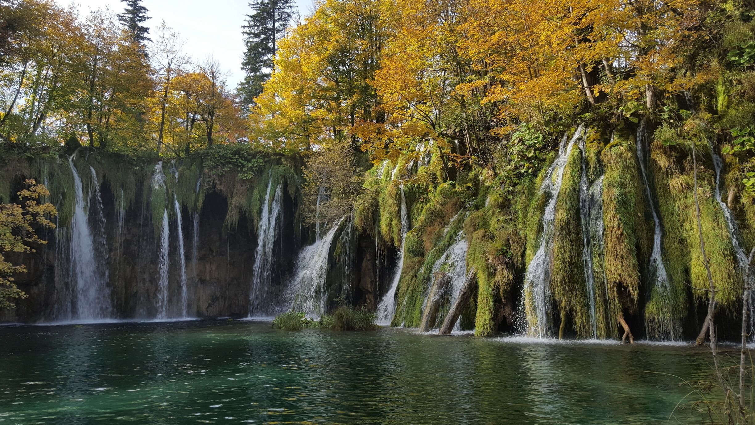 A waterfall cascading into a clear lake surrounded by autumn-colored trees.