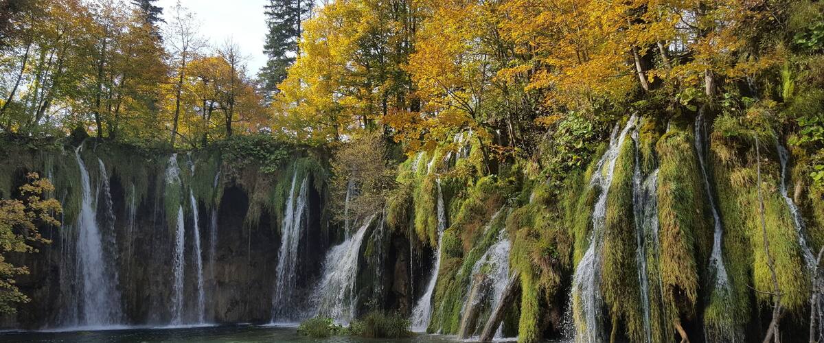 A waterfall cascading into a clear lake surrounded by autumn-colored trees.