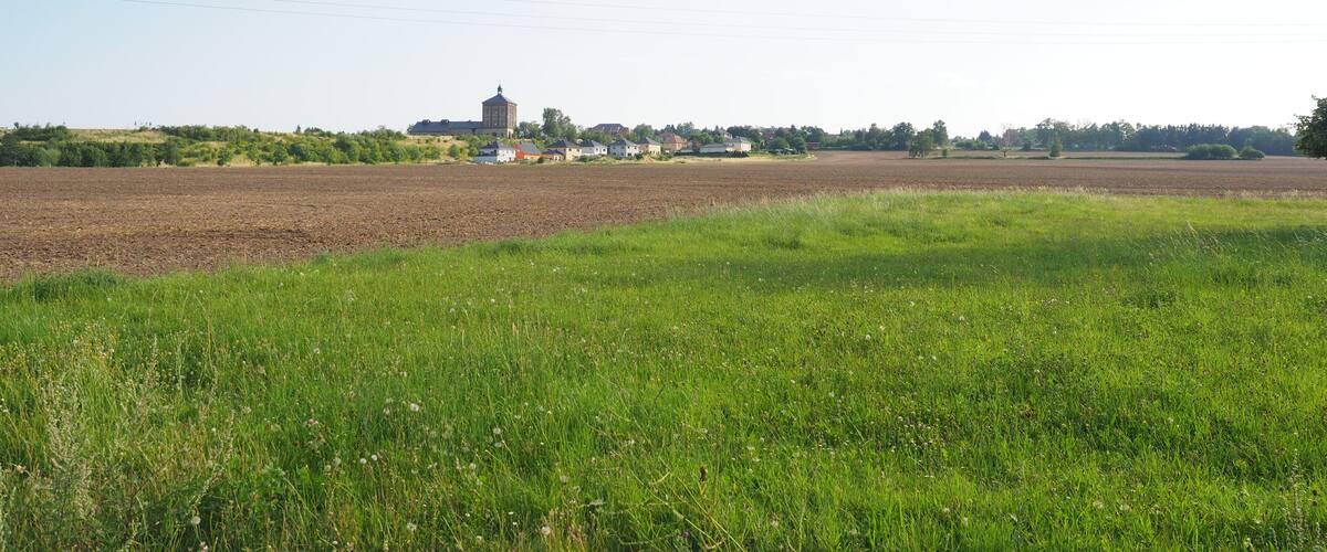 A rural landscape with a field, a small building, and a distant church.