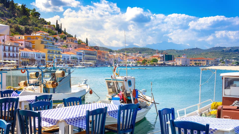 A harbor with boats, a table with blue and white checkered tablecloths, and buildings along the waterfront.