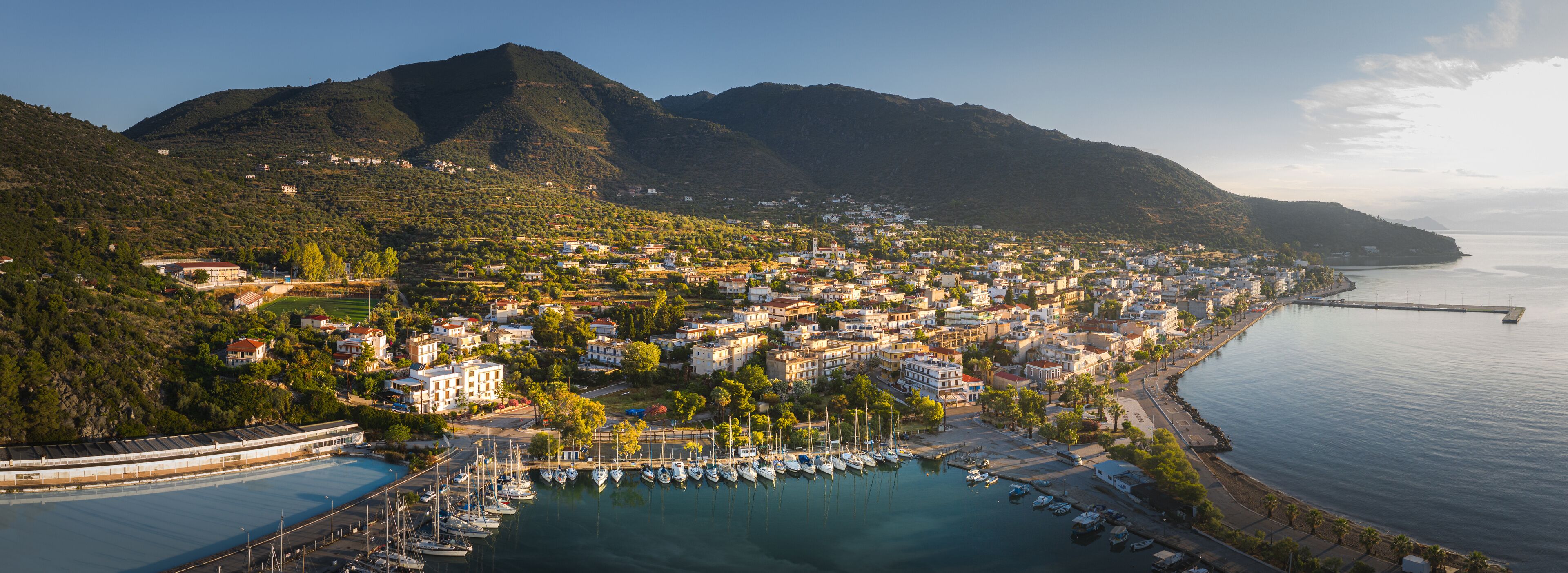 A coastal town with a marina, mountains in the background, and a clear sky.