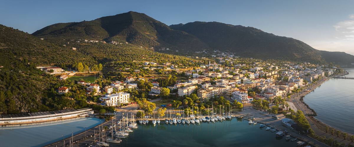 A coastal town with a marina, mountains in the background, and a clear sky.