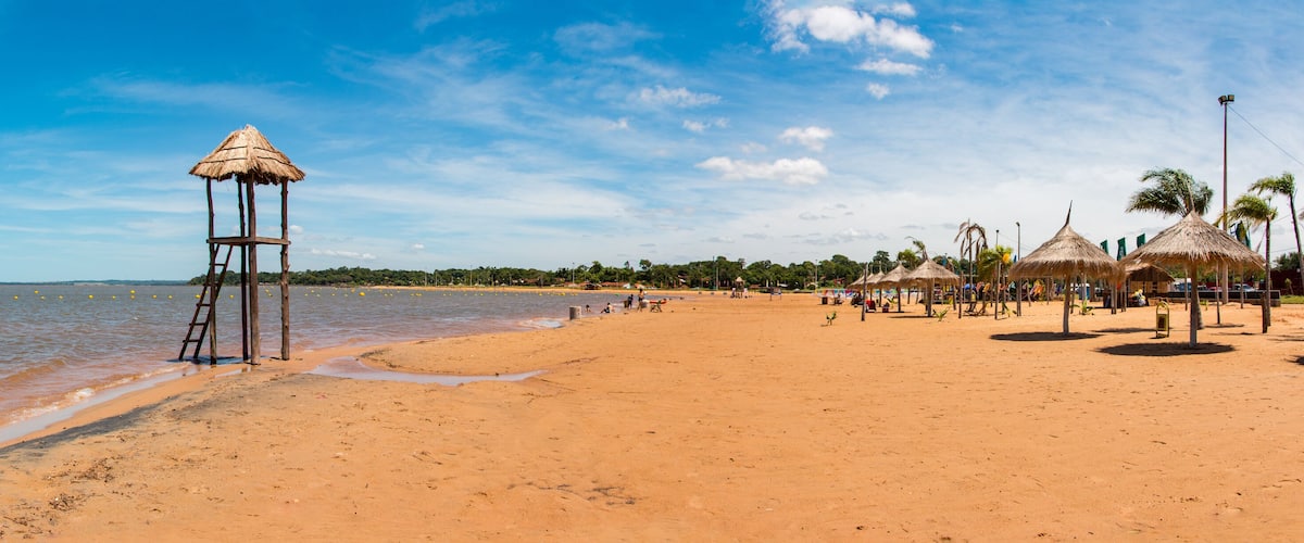 A beach with a thatched structure, palm trees, and a clear sky.