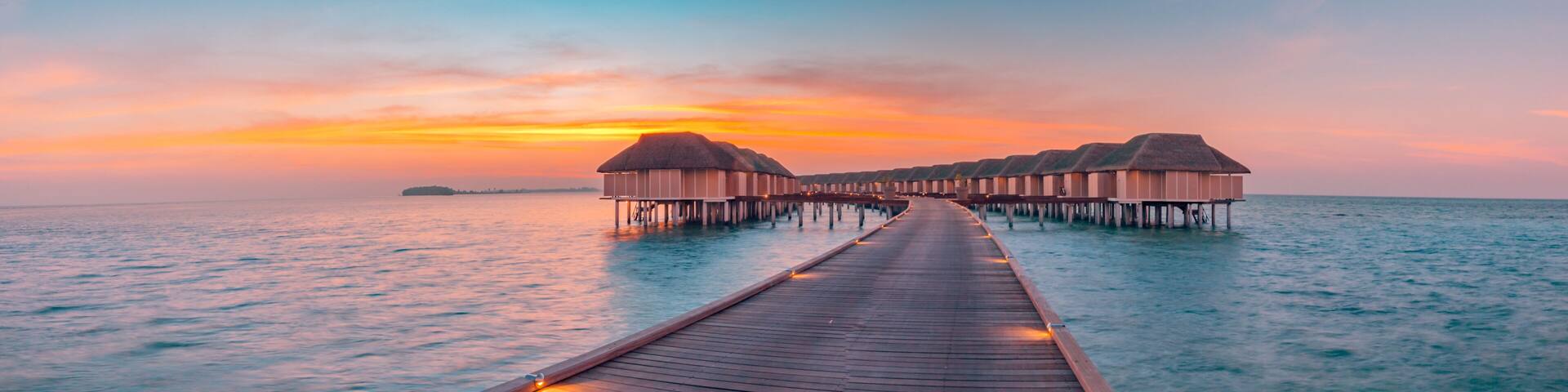 A wooden pier leading to overwater bungalows at sunset.