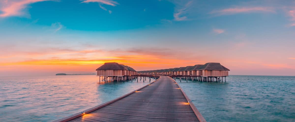 A wooden pier leading to overwater bungalows at sunset.