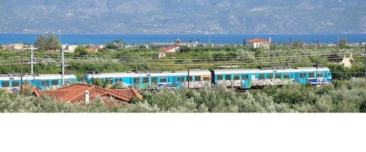 A train traveling through a rural area with mountains in the background.