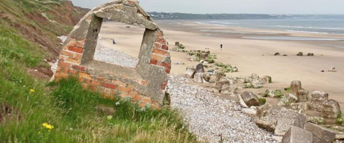 Une plage avec une structure en briques et un cerf-volant dans le ciel.