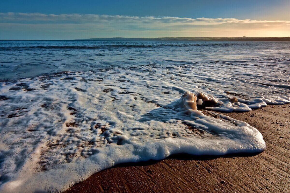 A beach with foamy waves and a clear sky.