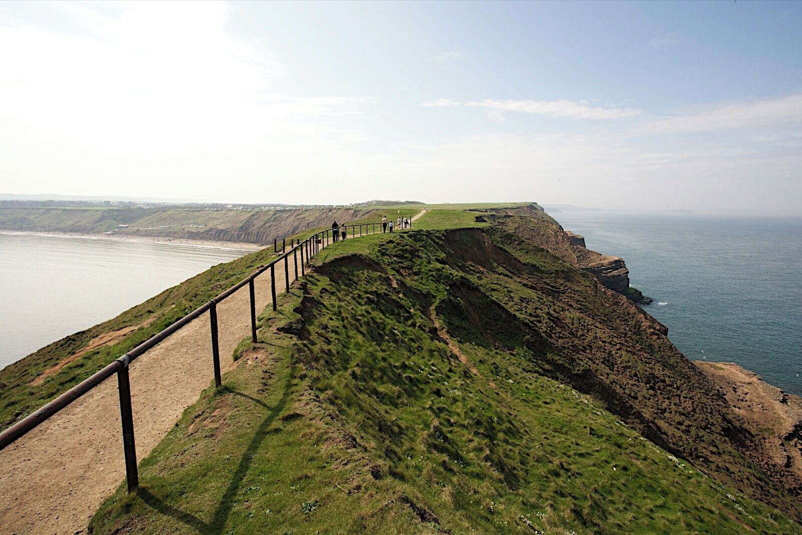 A coastal cliff path with a railing, overlooking the sea.