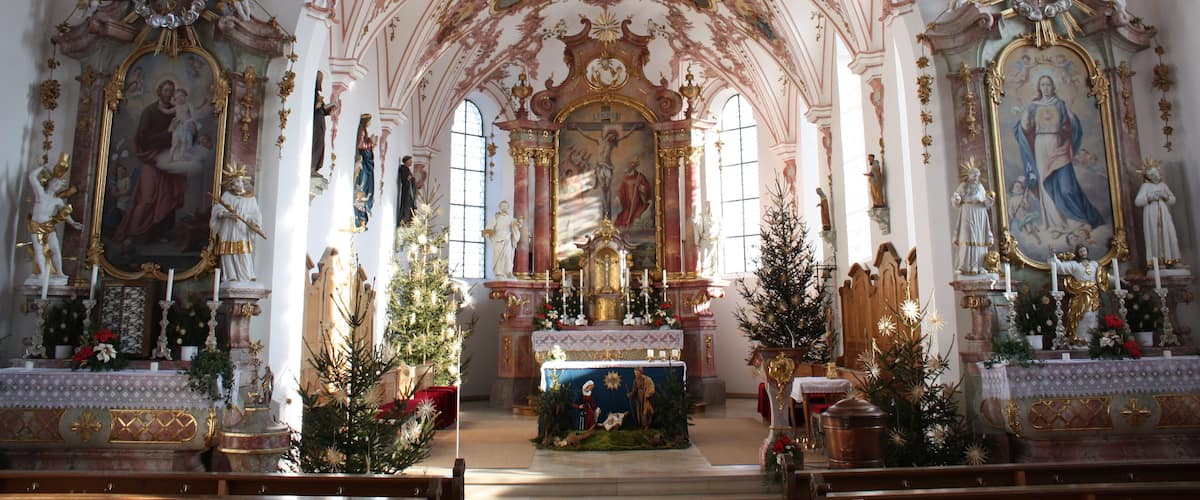 An ornate church interior with a high arched ceiling, religious paintings, and a central altar.