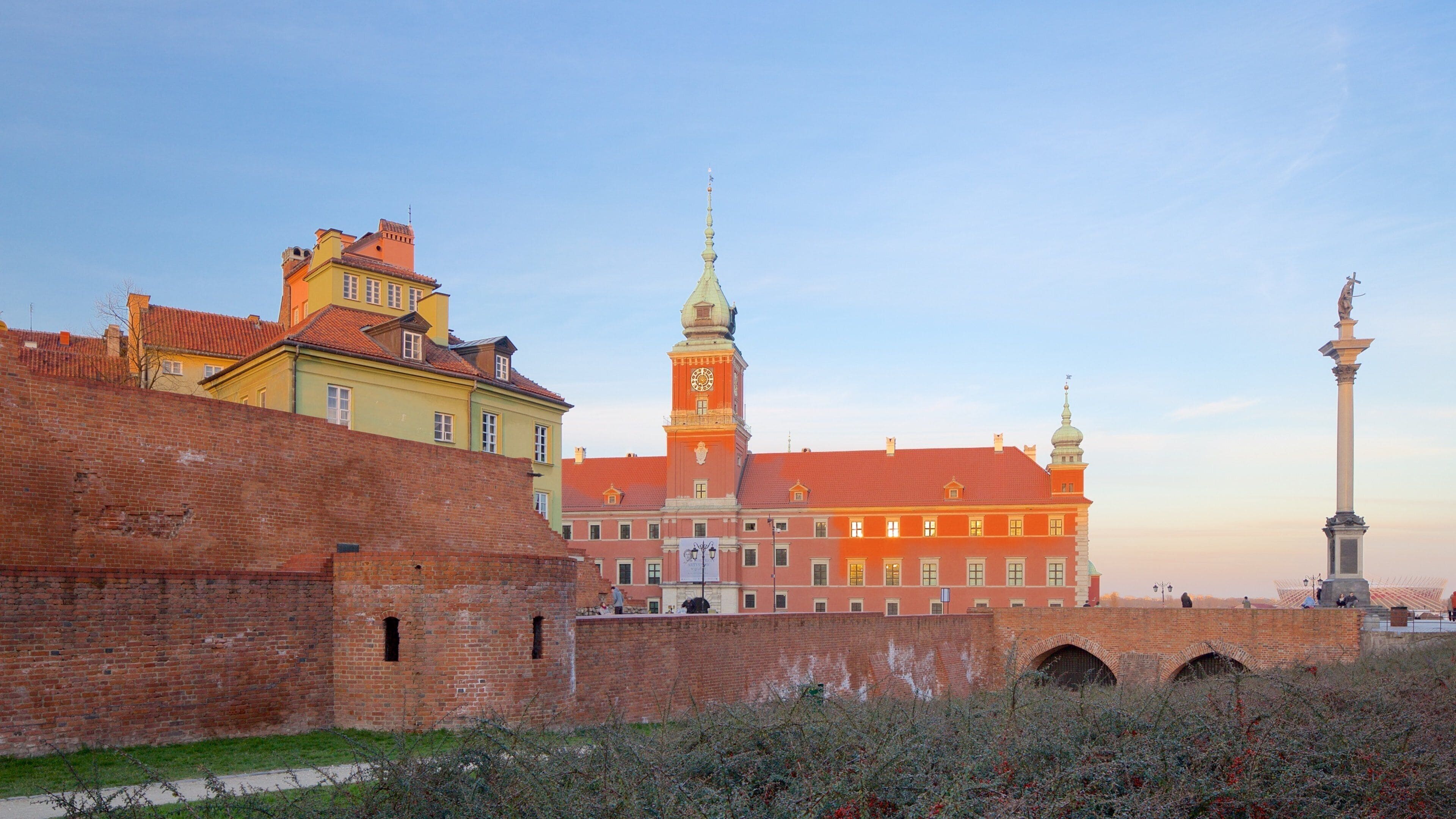 A historic building with a clock tower, a statue, and a brick wall.