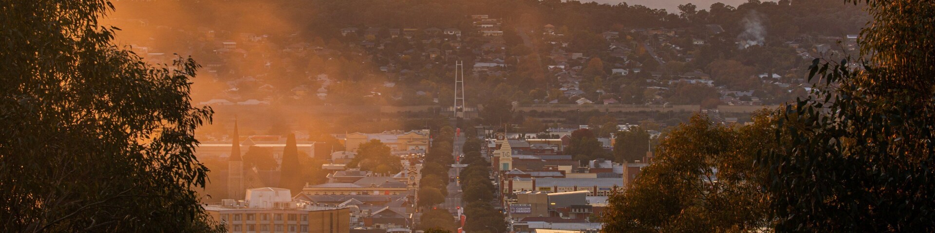 Paisagem urbana ao pôr do sol, com uma torre de igreja destacada e edifícios ao redor.