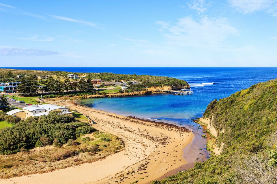A coastal landscape with a beach, houses, and a cliff overlooking the ocean.