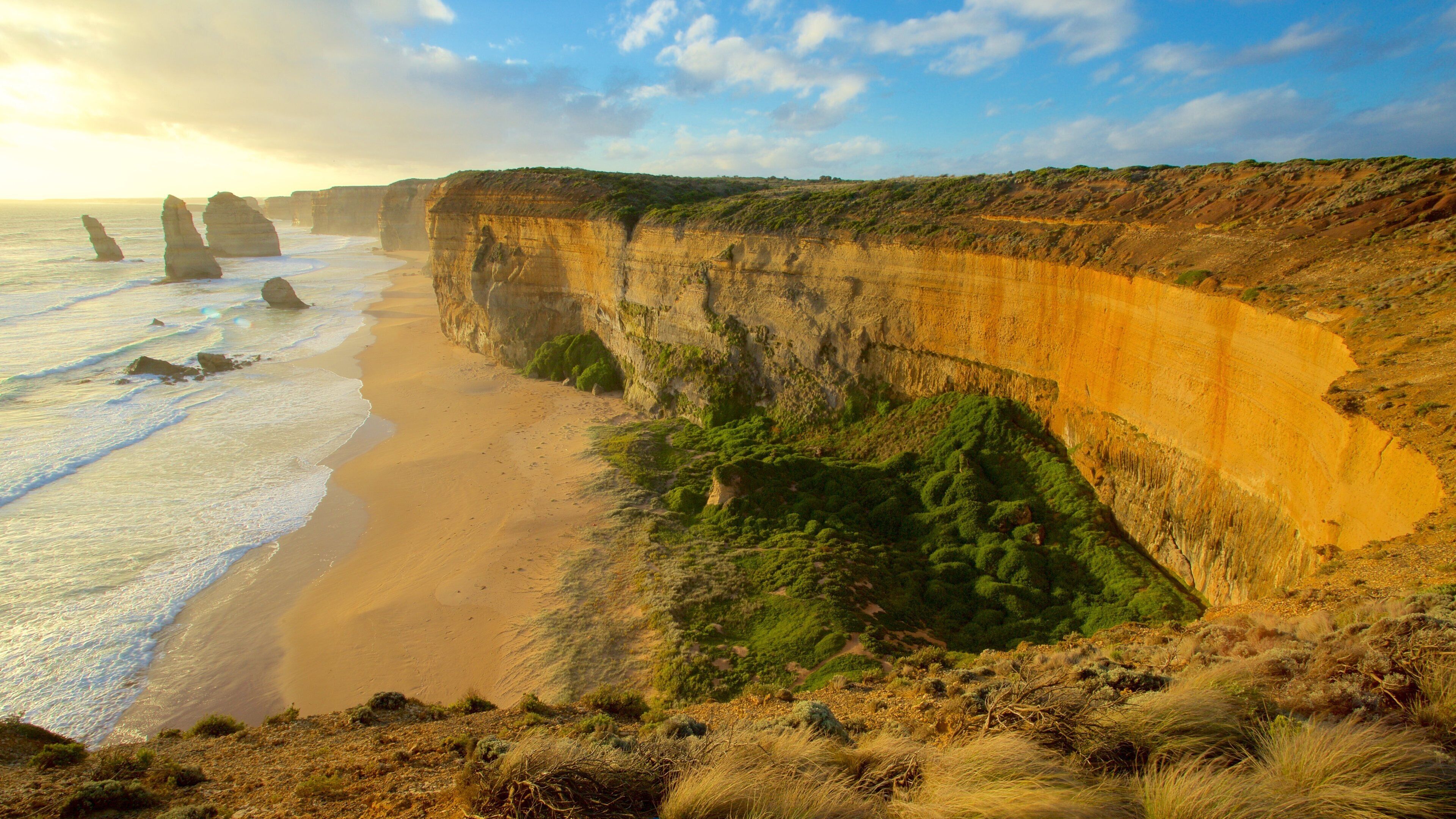 A coastal landscape with cliffs, a sandy beach, and waves.