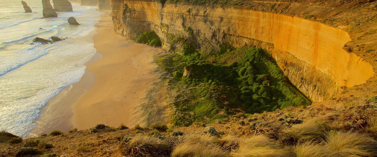 A coastal landscape with cliffs, a sandy beach, and waves.