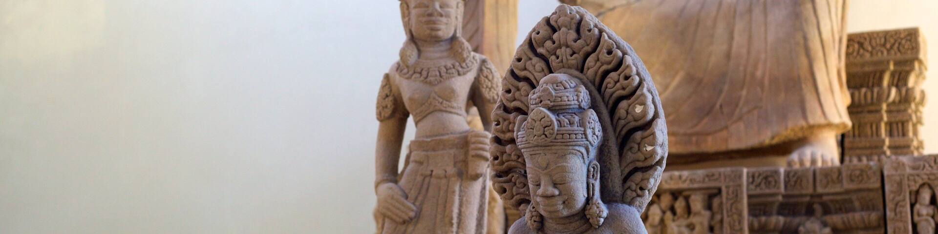 A collection of stone statues, including a seated figure and a standing figure with a headdress.