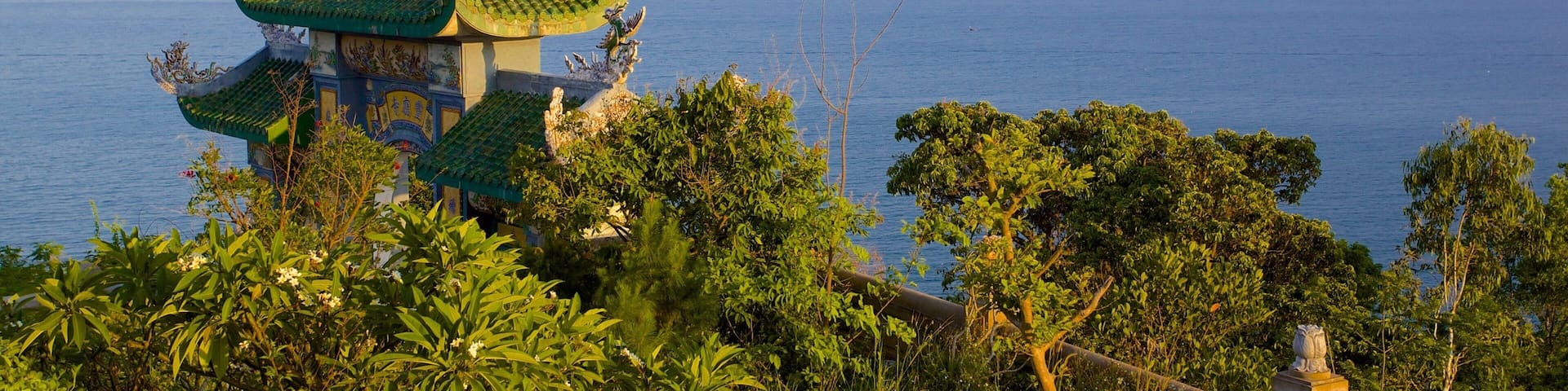 A traditional temple with ornate green roofs and golden decorations, overlooking a calm sea with a distant ship.