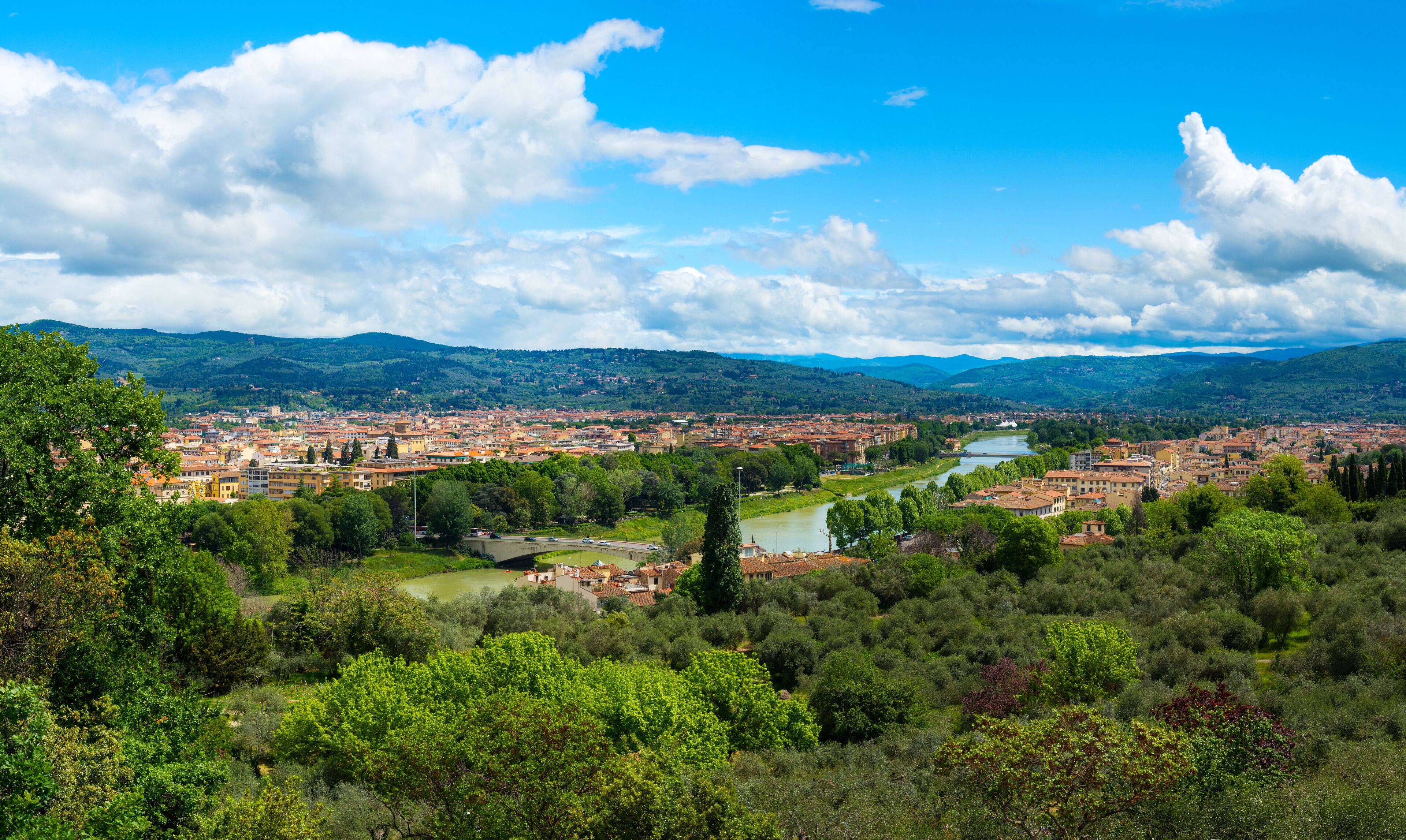 A city with a river, surrounded by mountains and greenery.