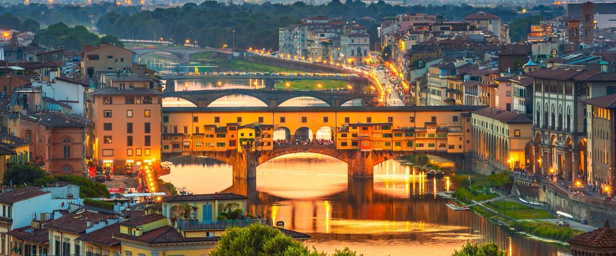 A cityscape with a prominent bridge over a river, surrounded by historic buildings and a distant mountain range.