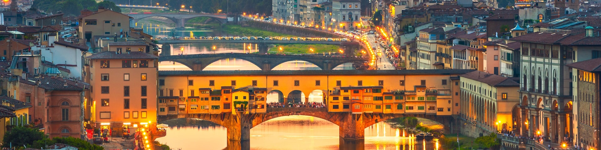 A cityscape with a prominent bridge over a river, surrounded by historic buildings and a distant mountain range.