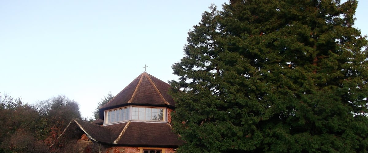 A brick house with a conical roof and a large tree in front.