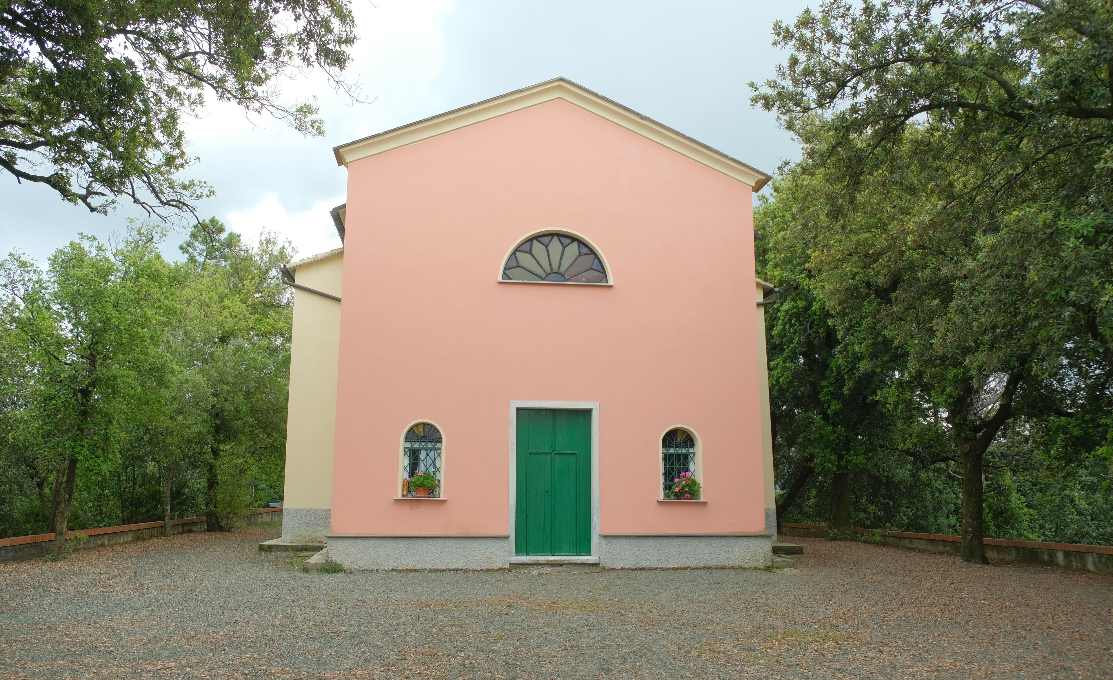 A pink building with a green door, two windows with flower boxes, and a curved window above the door.
