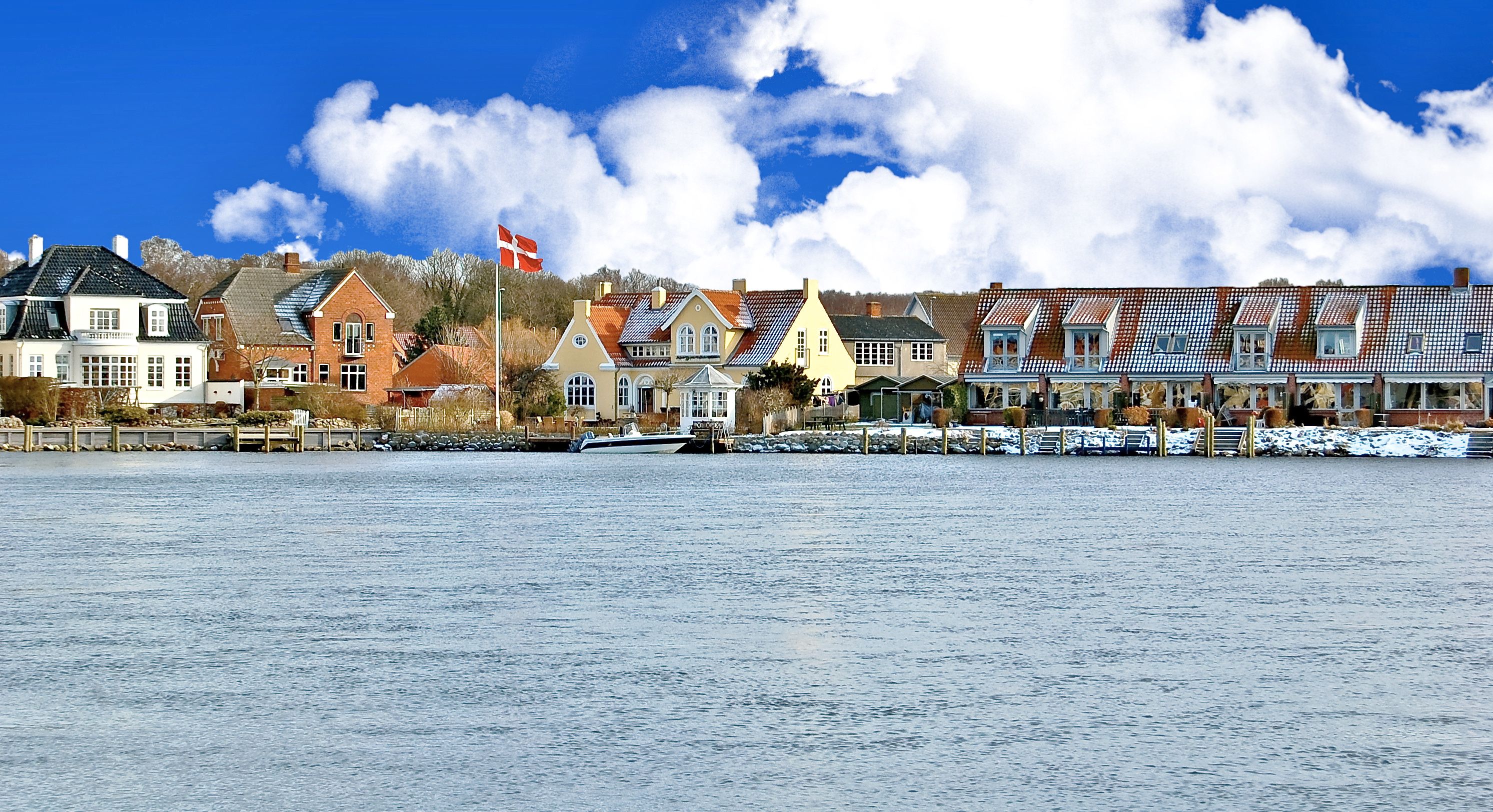 A waterfront town with traditional houses, a flag, and a boat docked by the water.