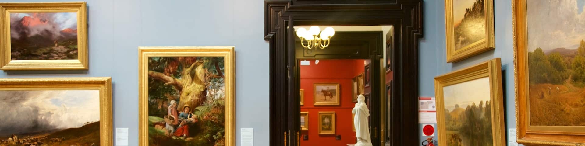 A gallery with large landscape paintings, a statue, and wooden furniture.