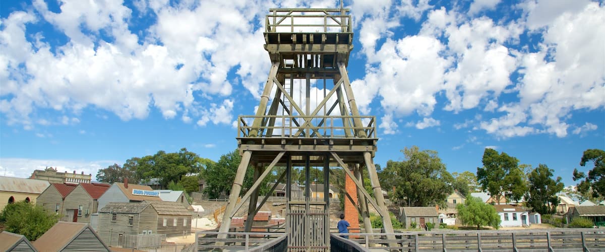 A historic mining tower with a flag, surrounded by old buildings and trees.