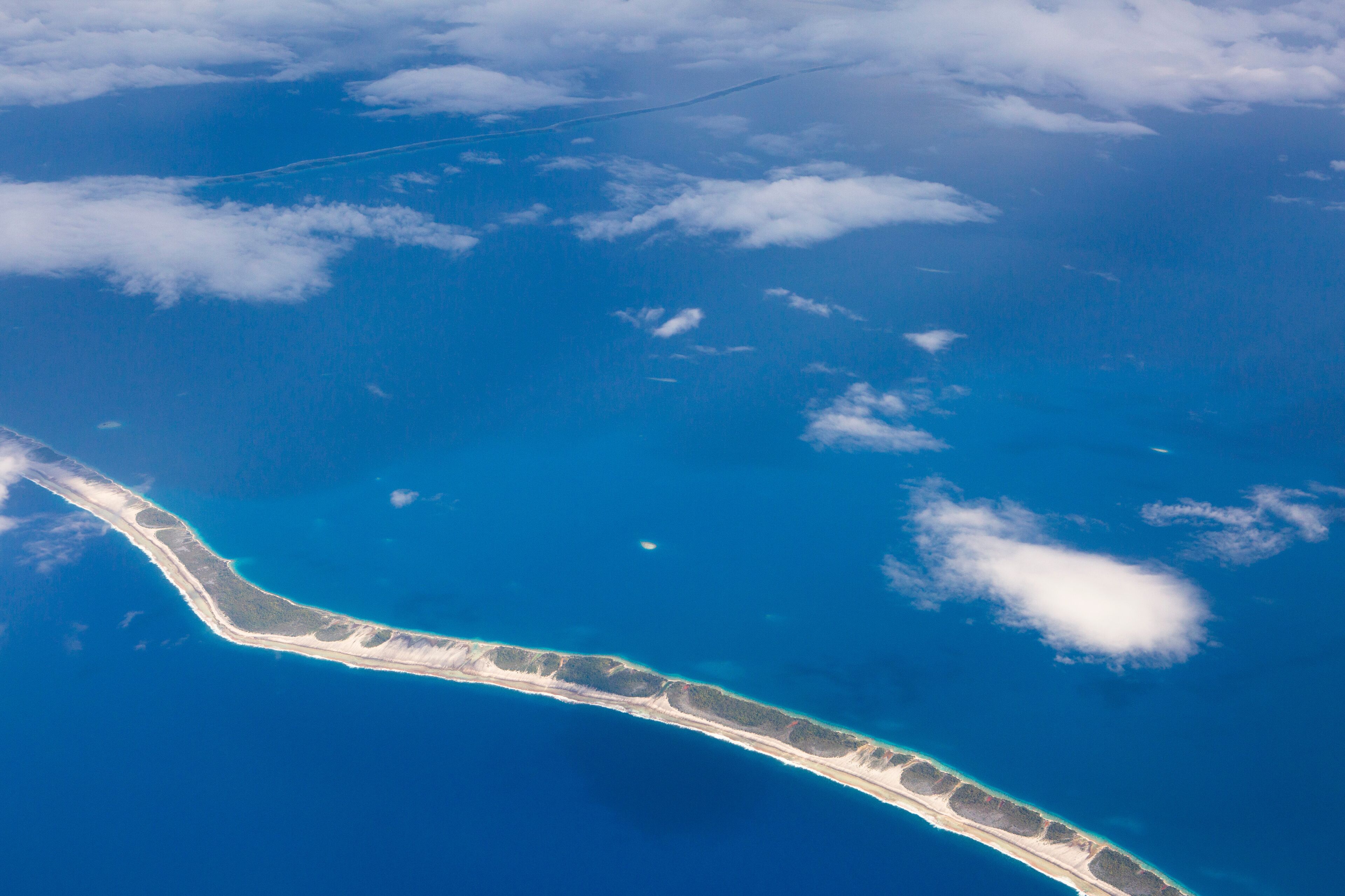 An aerial view of a narrow, elongated island with a clear blue ocean surrounding it.