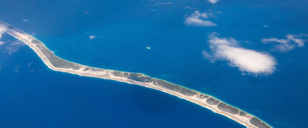 An aerial view of a narrow, elongated island with a clear blue ocean surrounding it.