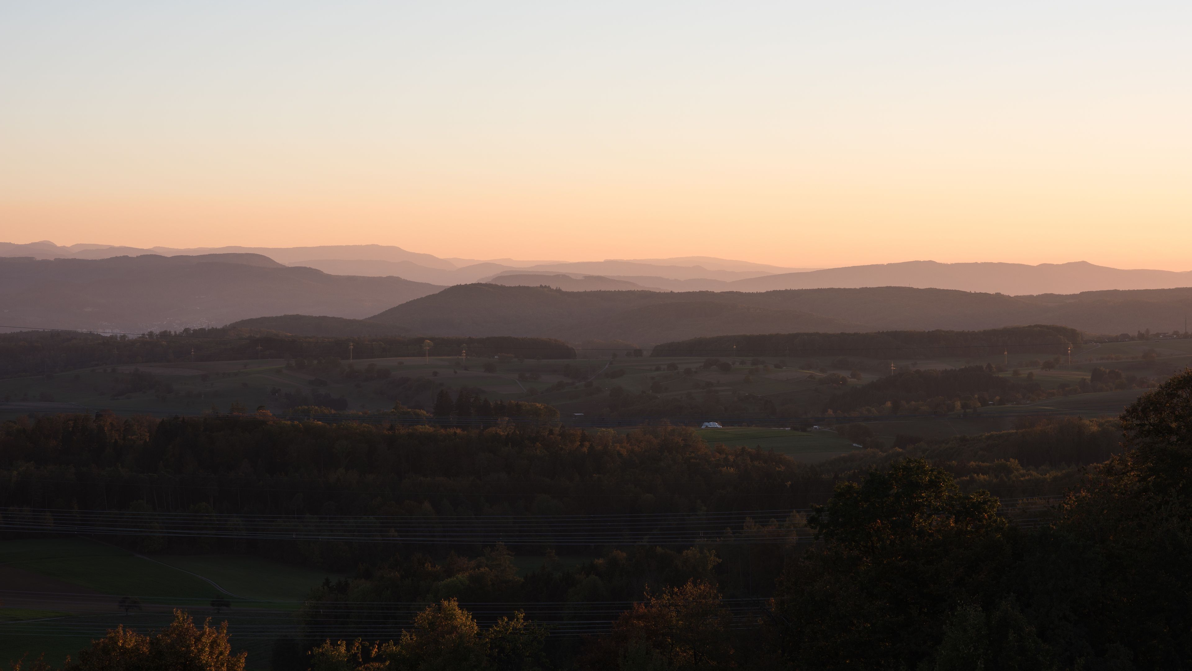 Une vallée aux collines douces, avec une chaîne de montagnes lointaine, au coucher du soleil.