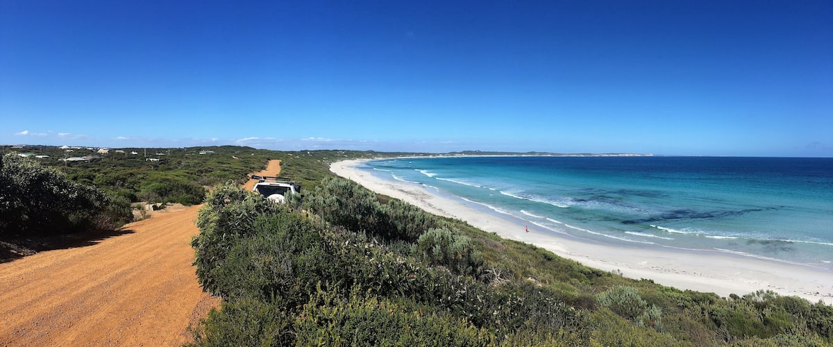 A coastal road leading to a beach with clear blue waters and green vegetation.