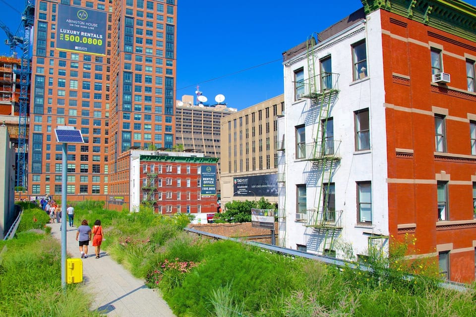 A cityscape with tall buildings, a red brick building with a fire escape, and a pathway with greenery.